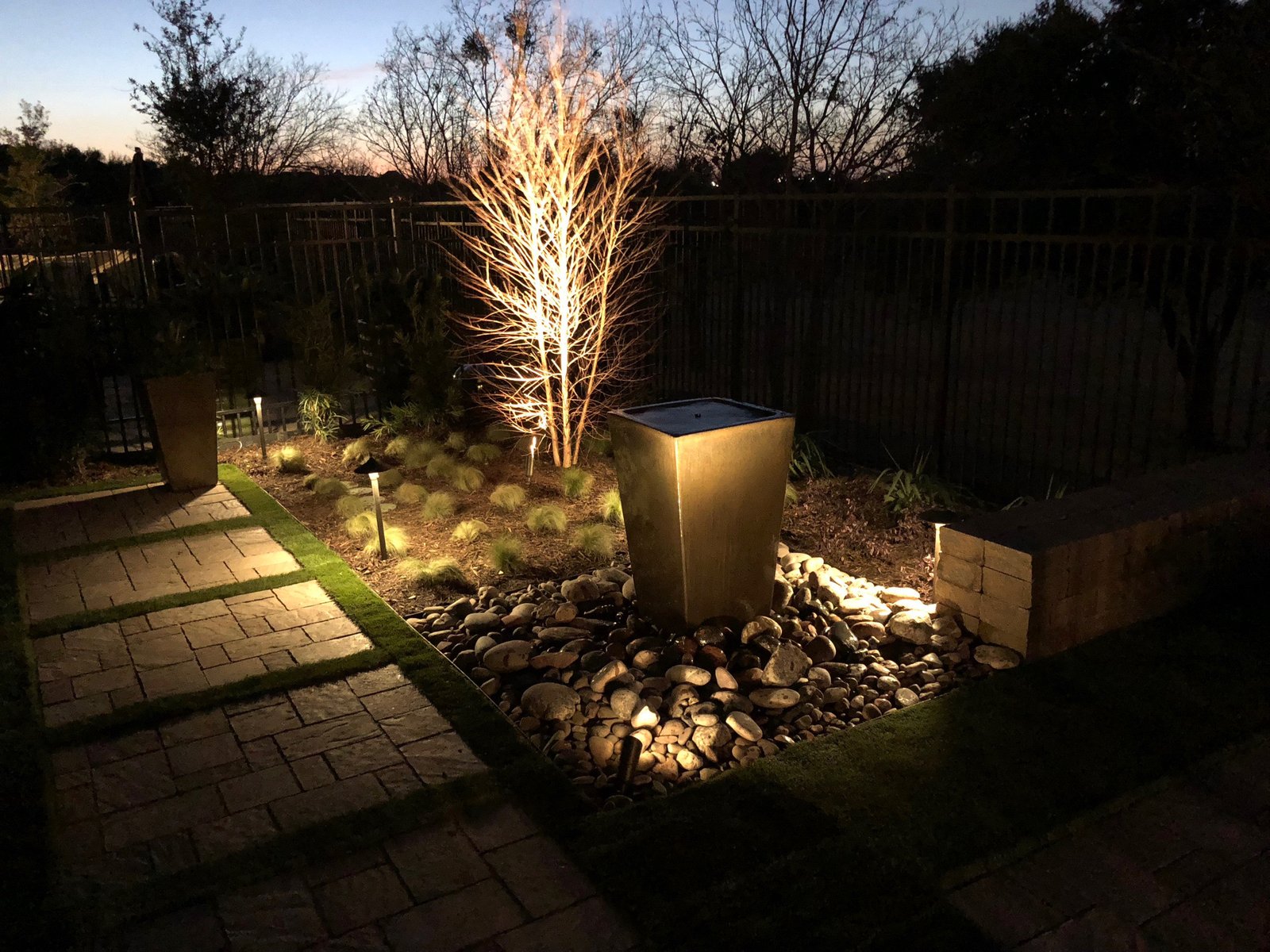 Uplit tree and water feature in a garden bed at night