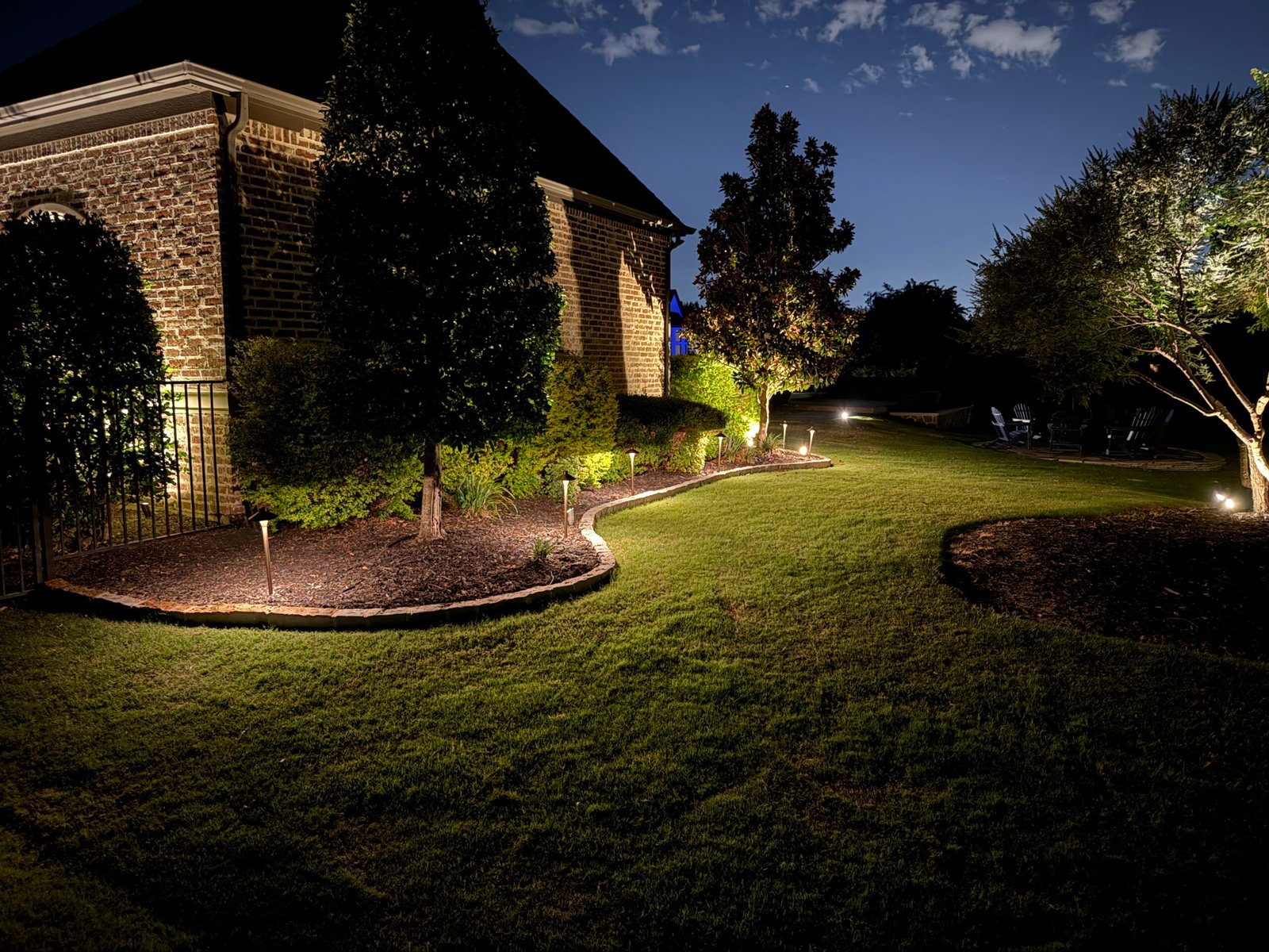 Landscape lighting on trees and flower beds in front of a home at dusk