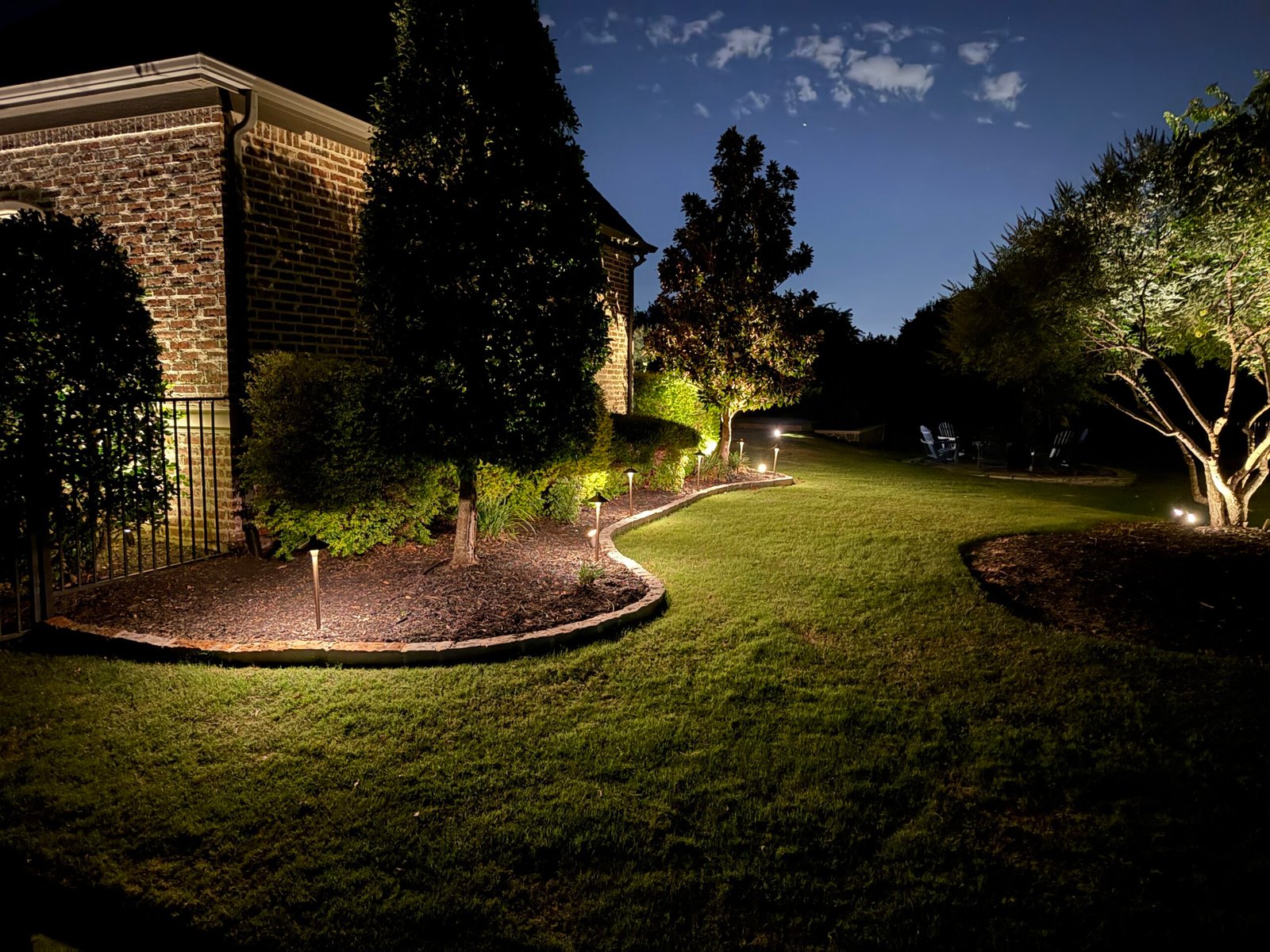 Landscape lighting on trees and curved bed edging in a backyard at night