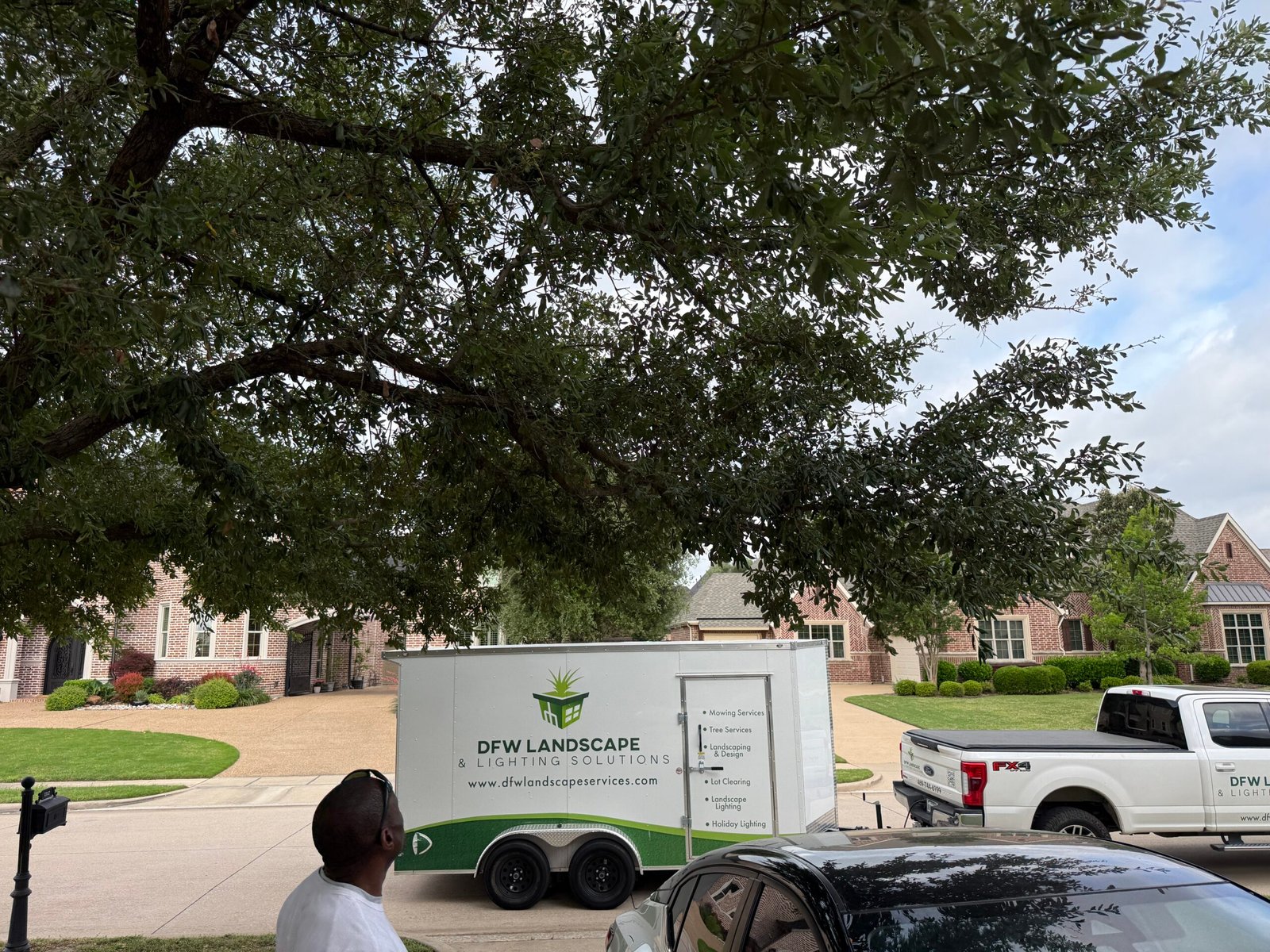 DFW Landscape & Lighting Solutions crew and trailer on a job under a large oak tree