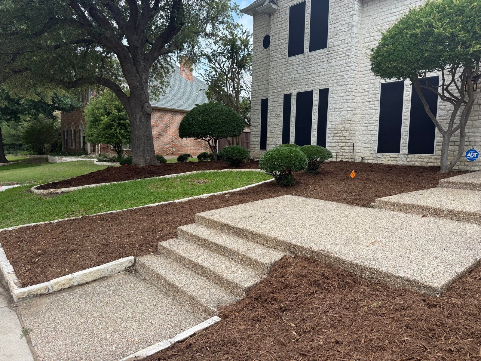 Fresh mulch beds and gravel path beside the front steps of a two-story home
